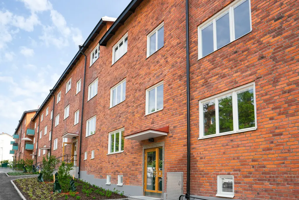 Flerbostadshus i rött tegel med gräsmatta och gångväg